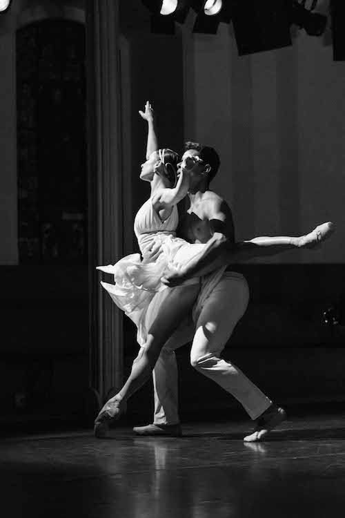 A woman in Grecian-inspired costume executes an arabesque en pointe while her maie partner supports her at the waist